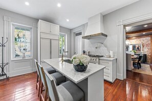 A modern kitchen with white cabinetry, a central island with bar stools, a gas stove, and a large window providing natural light. - Rare, Historical Estate near Market St w. Parking (Charleston)