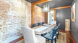 A dining area with a rustic brick wall, wooden beams, and a long wooden table with chairs. - Rare, Historical Estate near Market St w. Parking (Charleston)