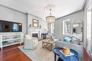 A living room with a fireplace, a television, and a chandelier. - Rare, Historical Estate near Market St w. Parking (Charleston)