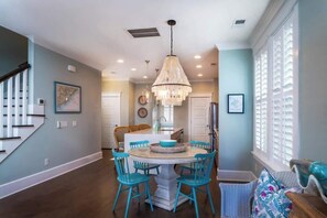 A dining area with a round table, blue chairs, a chandelier, and a view of a staircase. - Cozy 3 Bedroom Home Near Sullivans Island (Mount Pleasant)