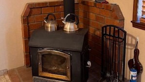 Een houtkachel met twee theepotten erop, een schoorsteen en een gasfles in de buurt.