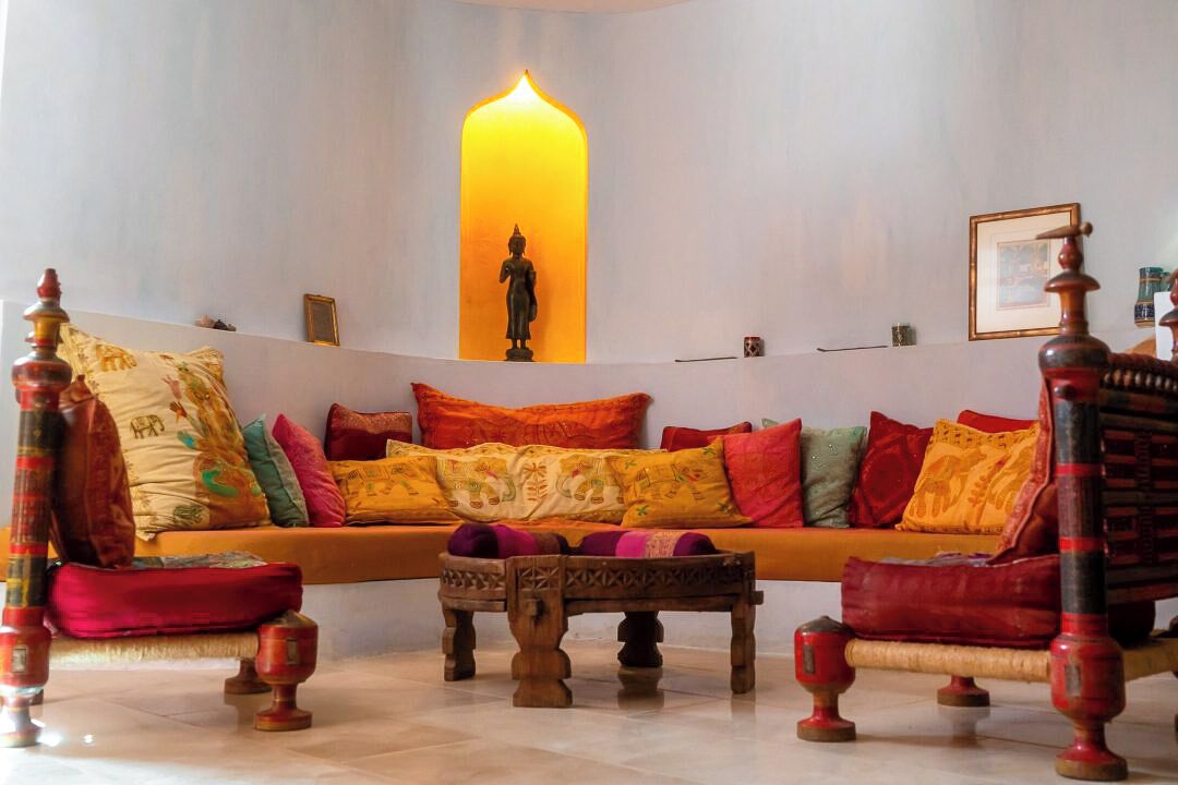 A living room with a sofa, wooden chairs, a small table, and a wall-mounted candle.