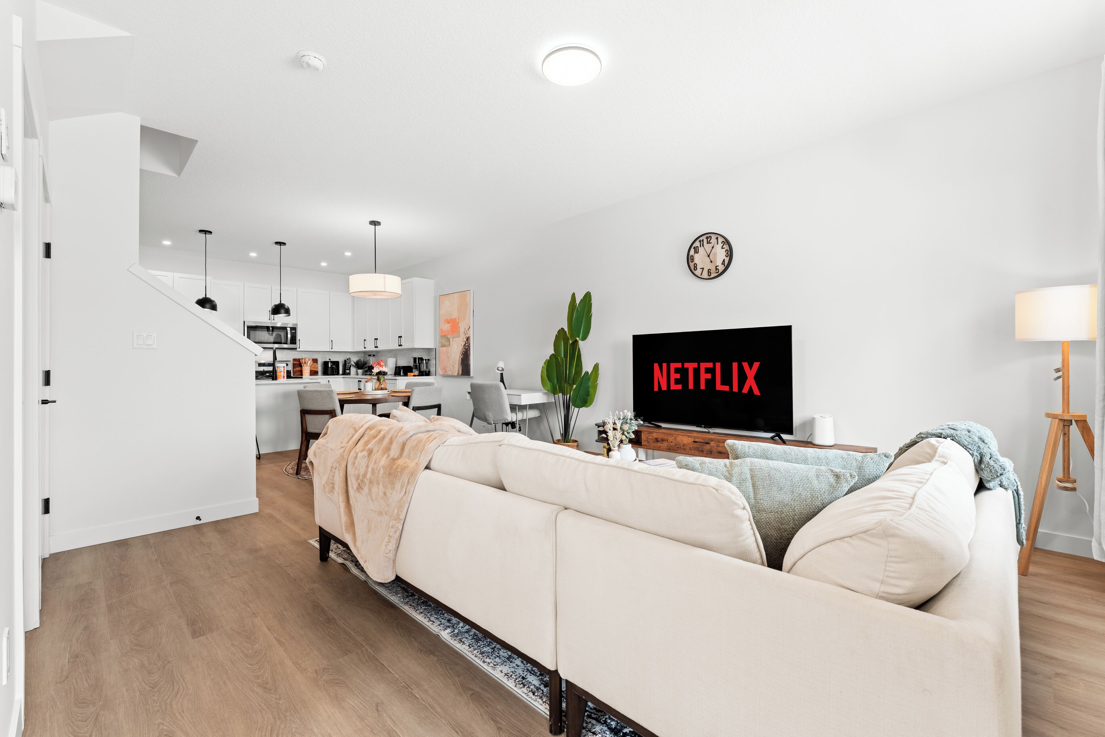 A modern living room with a sofa, a TV displaying 'NETFLIX', and a staircase leading to a kitchen.