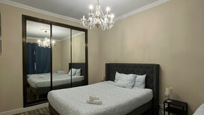 A hotel room with a large bed, a mirror, a chandelier, and a small bedside table.