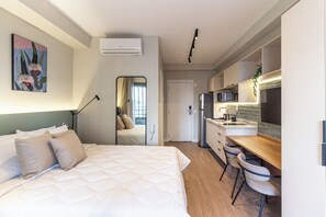 A modern hotel room with a bed, bedside lamp, air conditioning unit, and a view of the kitchen area. - 360 Latitude Campo Belo  (São Paulo)