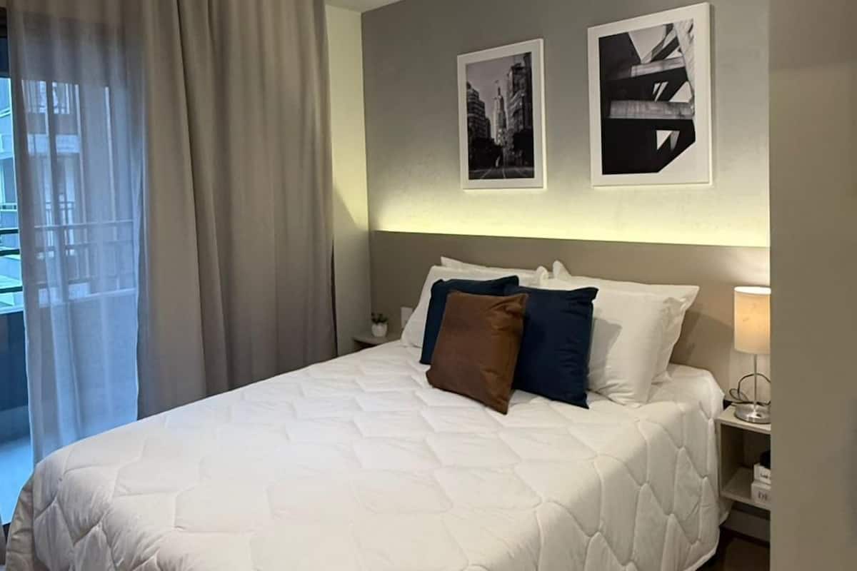 Una habitación de hotel moderna con una cama grande, una mesita de noche, una lámpara y dos cuadros en la pared.