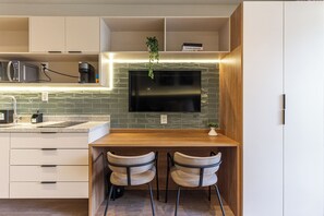 A modern kitchen with a built-in TV, wooden countertop, two bar stools, and a microwave. - 360 Latitude Campo Belo  (São Paulo)