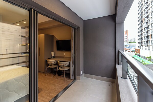 A modern apartment with a balcony, a dining area with two chairs, a flat-screen TV mounted on the wall, and a view of the cityscape. - 360 Latitude Campo Belo  (São Paulo)