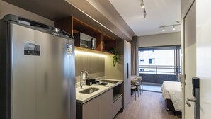 Et moderne køkken med køleskab, vask og bordplade. Der er en seng med hvidt sengetøj og en balkon med gelænder.