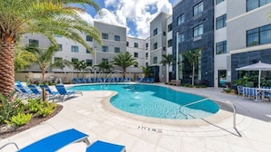 A swimming pool with blue lounge chairs, palm trees, and a modern building with multiple floors and large windows. - Accessible 2BR Pool-View Family Suite in Naples (Naples)