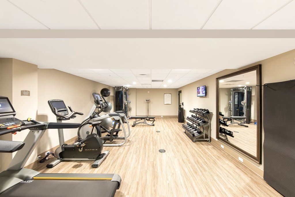 Ein Fitnessraum mit Laufbändern, Kraftbänken und Spiegeln.