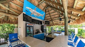 Un restaurante con techo de paja, sillas azules y un gran mural de un tiburón en la pared.