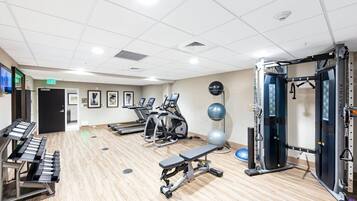 A gym with cardio machines, weightlifting equipment, and a bench.