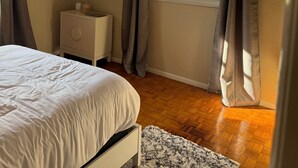 Una camera da letto con un letto, una ventola a soffitto, una televisione, una finestra con tende e un pavimento in legno.
