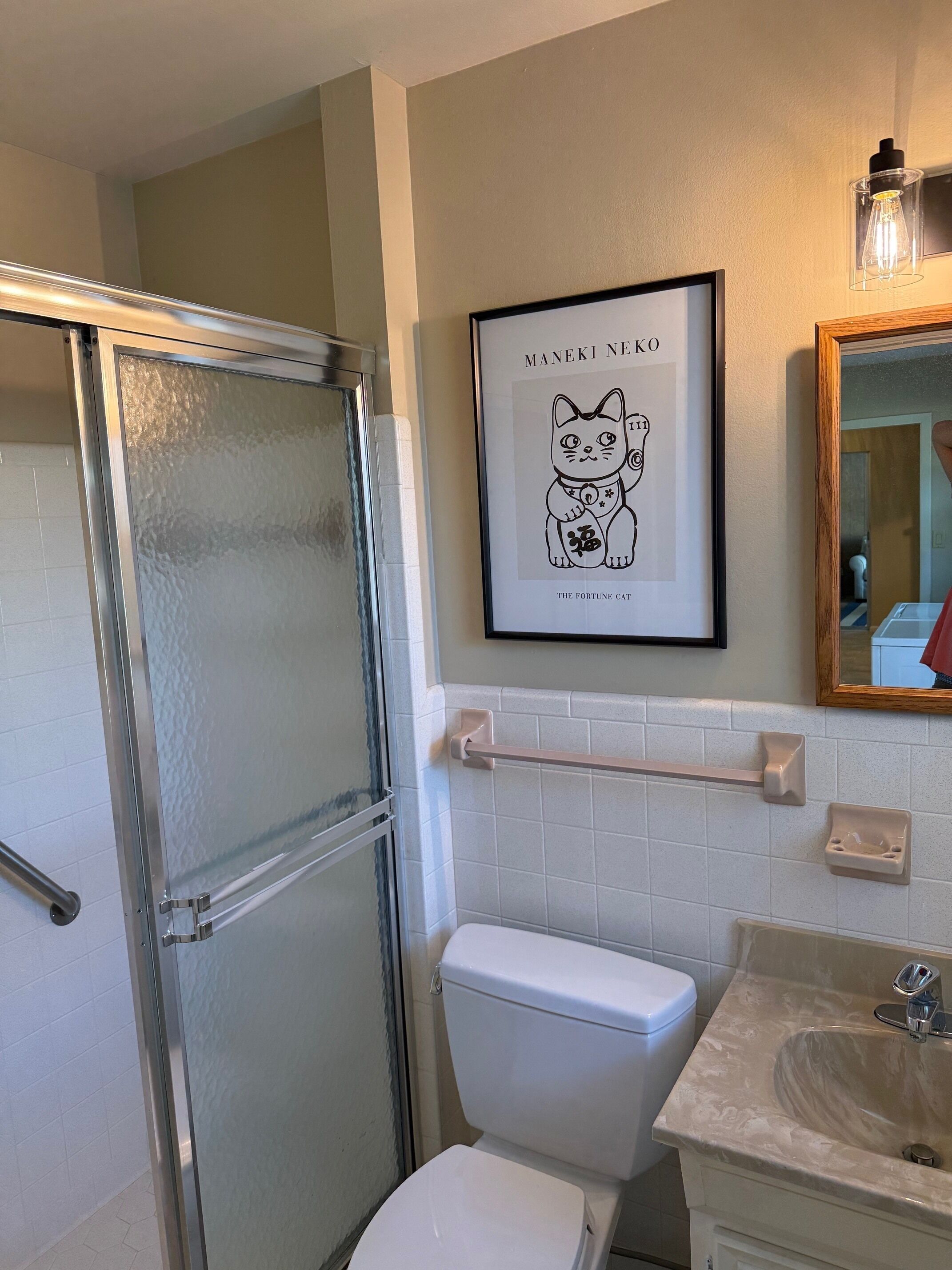 Een badkamer met een douchecabine van glas, een wit toilet, een wastafel met een marmeren blad en een fotokader met een kat aan de muur.
