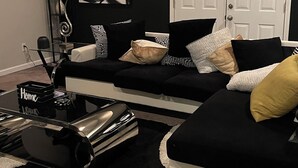 Ein modernes Wohnzimmer mit einem schwarz-weißen Sofa, einem Glastisch und einem großen, abstrakten Gemälde an der Wand.