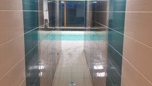 Un área de piscina interior moderna con paredes de vidrio y suelo de baldosas.