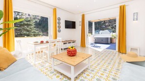 Una habitación moderna con una mesa de madera, sillas blancas, un sofá y un ventanal con cortinas.