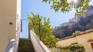 Una escalera conduce a un edificio de fachada blanca, con barandilla metálica y vistas a una colina con edificios.