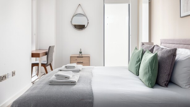 Quarto de hotel com cama, escrivaninha, cadeira, cômoda e espelho.
