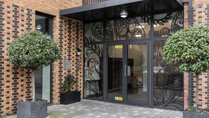 Um edifício de tijolos com entrada por porta de vidro, dois vasos de plantas e calçada de azulejos.