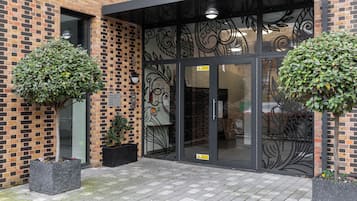Un edificio de ladrillo con entrada de puerta de cristal, dos macetas y pavimento de baldosas.