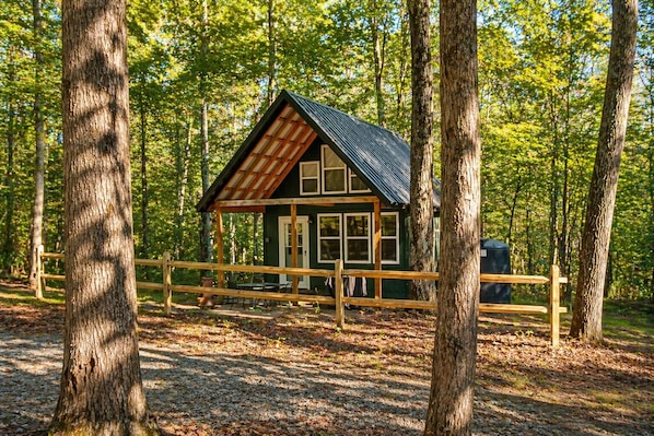 A cabin with a sloped roof, wooden deck, and a fenced area.