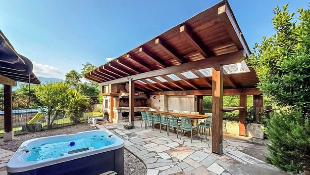 A covered outdoor patio with a hot tub, stone flooring, and a barbecue area.