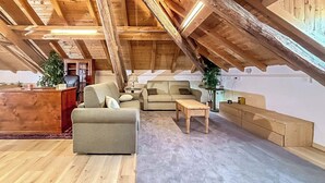 A spacious attic room with a wooden ceiling, a desk, two sofas, a small table, and a potted plant.