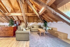 A spacious attic room with a wooden ceiling, a desk, two sofas, a small table, and a potted plant. - Villa al Lago - Where the Dolomites meet Lake Santa Croce (Lizzona)