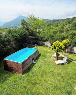 Ein rechteckiger Swimmingpool mit Steinbord, einer überdachten Terrasse und einem Liegestuhl.