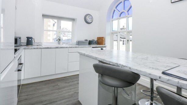 Une cuisine moderne avec des meubles blancs, un plan de travail en marbre et une horloge au mur.