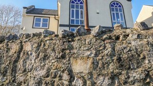 Un bâtiment avec un mur en pierre au premier plan et un toit à deux versants surmonté d’une cheminée.