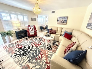 Un salon avec un canapé beige, un fauteuil rouge, un tapis à motifs et un lustre.