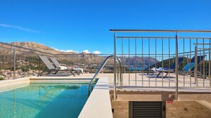 Una piscina con barandilla de metal, sillas de descanso y vistas a montañas al fondo.