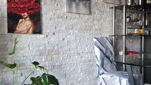 Een moderne woonkamer met een gestructureerde stenen muur, een glazen salontafel, een blauw tapijt en een potplant.