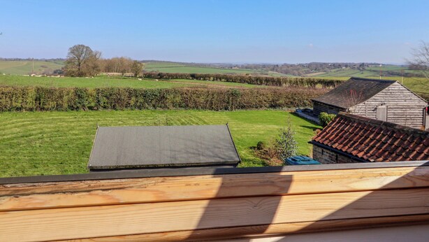 A view from a window overlooking a rural landscape with fields, a hedge, and a wooden building. - Brush and Boot (York)