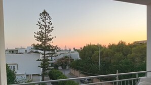 Ein Balkon mit Tisch und Stühlen, der einen Wohnbereich mit Häusern und Bäumen im Abendlicht zeigt.