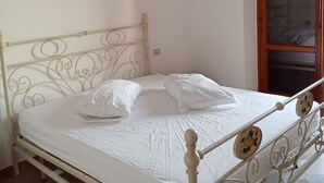 Ein Bett mit Metallgestell und weißer Bettwäsche, ein Gemälde an der Wand und eine Holztür.
