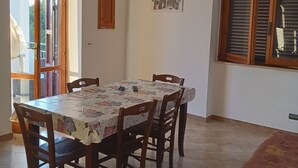Ein Essbereich mit Tisch für vier Personen, umgeben von Holzstühlen, einem Fenster mit Jalousien und einer Tür, die nach draußen führt.