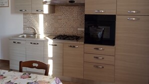 Eine Küche mit hellen Holzschränken, einem Gasherd, einem eingebauten Backofen und einer gefliesten Spritzschutzwand.