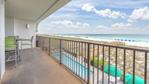 Un balcón con vista a la playa, una piscina y sillas de playa.