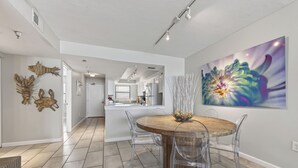 Cocina moderna con armarios blancos, una isla central y un comedor con mesa de madera y sillas transparentes.