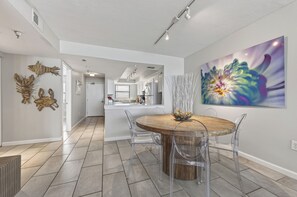 Eine moderne Küche mit weißen Schränken, einer zentralen Kochinsel und einem Essbereich mit Holztisch und transparenten Stühlen.
