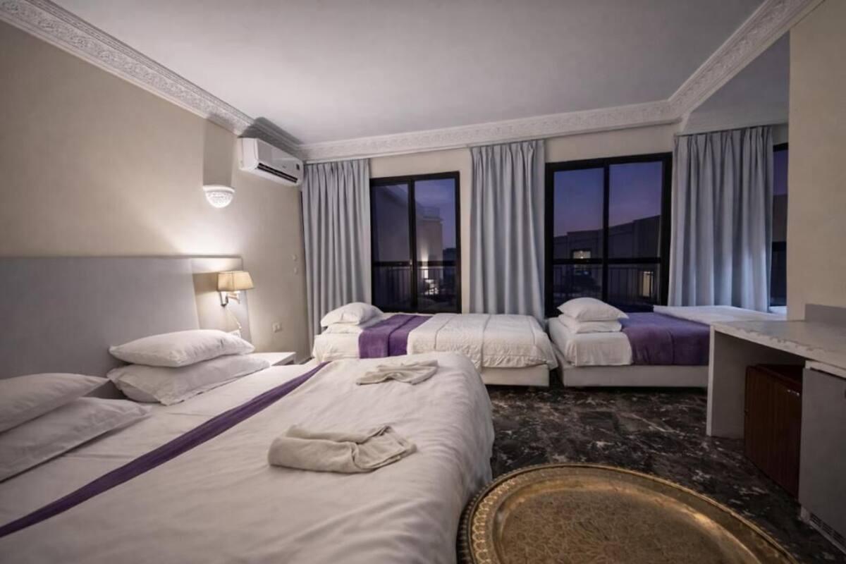 Une chambre d’hôtel avec deux lits, un bureau, un miroir et une vue sur la ville au crépuscule.