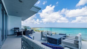 Un balcón con mobiliario exterior, un sofá y una mesa, con vistas a un mar azul turquesa y a una playa.