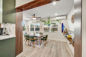 Un comedor con una mesa y sillas, un ventilador de techo y plantas colgantes.