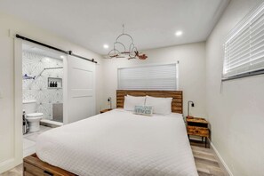 Un dormitorio con una cama grande, cabecera de madera, mesita de noche con lámpara, y una lámpara de pared.