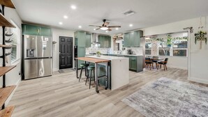 A modern kitchen with a central island, stainless steel appliances, and a dining area with a table and chairs. - Canal Side Cocoa Beach 3BR 3BA Retreat (Cocoa Beach)