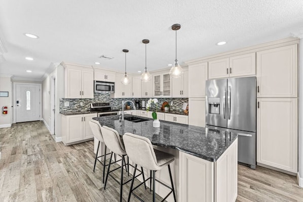 A modern kitchen with white cabinets, a granite countertop, stainless steel appliances, and bar stools.